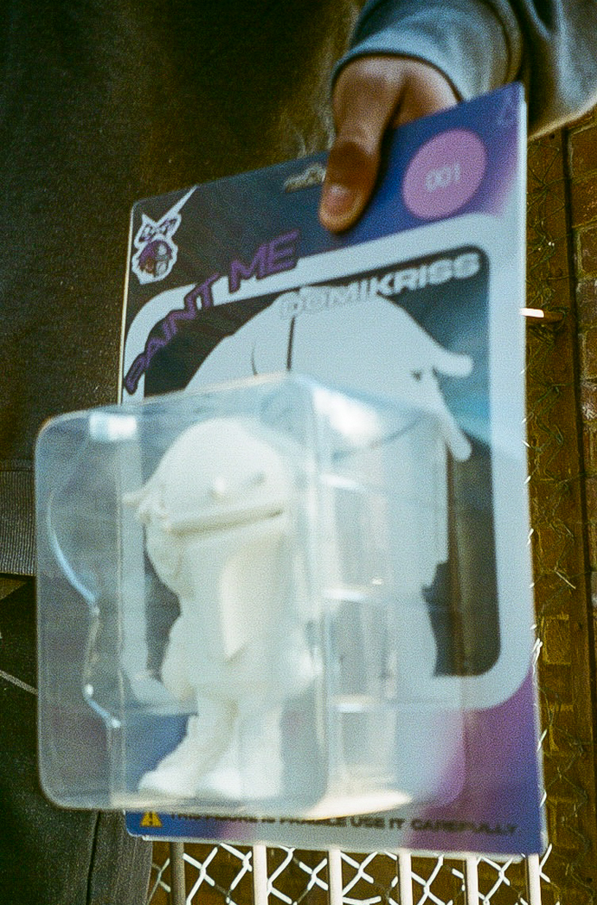 DomiKriss standing, holding 3D printed design object in blister pack, wearing colorfully designed helmet